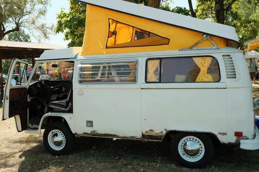 A white VW Westfalia camper with its yellow pop-top raised and the driver's door open
