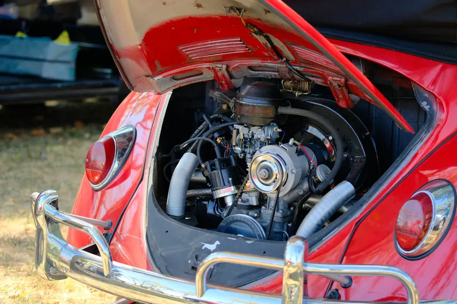 The air-cooled engine of a red Beetle, deck lid up, behind a chrome bumper